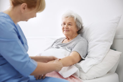 Caregiver massaging hand of senior woman on bed